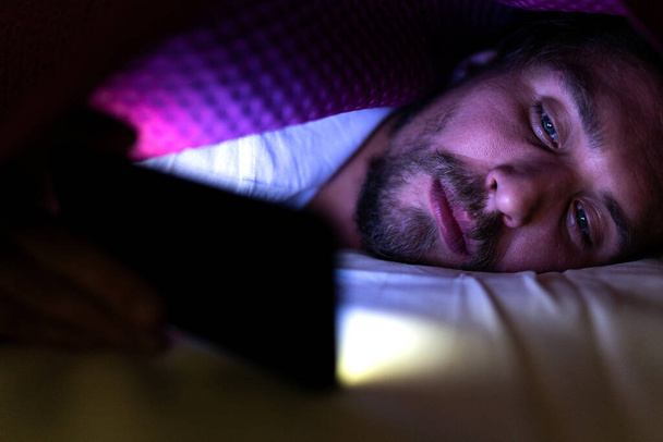 Бородатый молодой человек лежит в постели под одеялом. Он не может
 - Фото, изображение