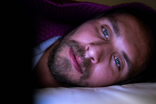Бородатый молодой человек лежит в постели под одеялом. Он не может
 - Фото, изображение