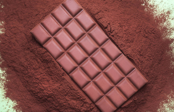 Milk chocolate bar on a cocoa powder pile. Chocolate ingredients - Photo, Image