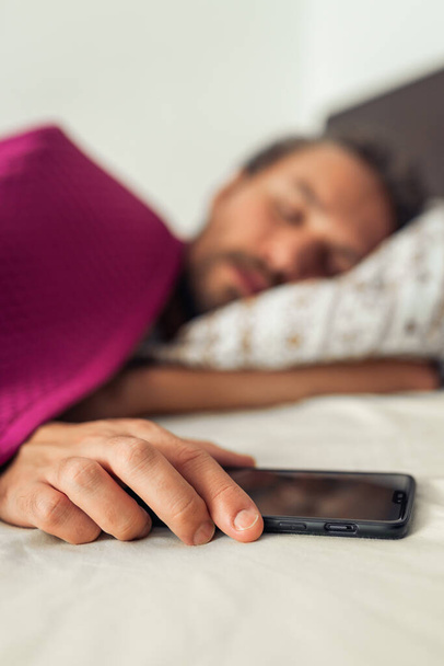 Sleeping young handsome man while holding his mobile phone. Scre - Фото, изображение