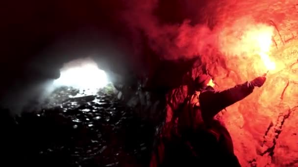 Homem solitário com uma chama de sinal de queima vermelha em uma caverna escura à procura do buraco, conceito de turismo. Imagens de stock. Masculino explorando caverna subterrânea
. - Filmagem, Vídeo