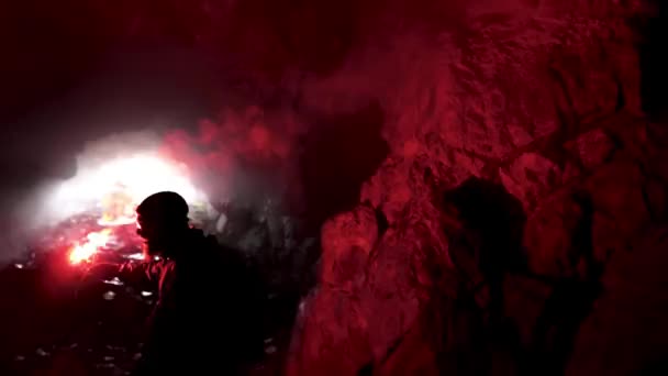 Hombre solitario con una llamarada de señal roja en una caverna oscura buscando el agujero, el concepto de turismo. Imágenes de archivo. Hombre explorando cueva subterránea
. - Metraje, vídeo