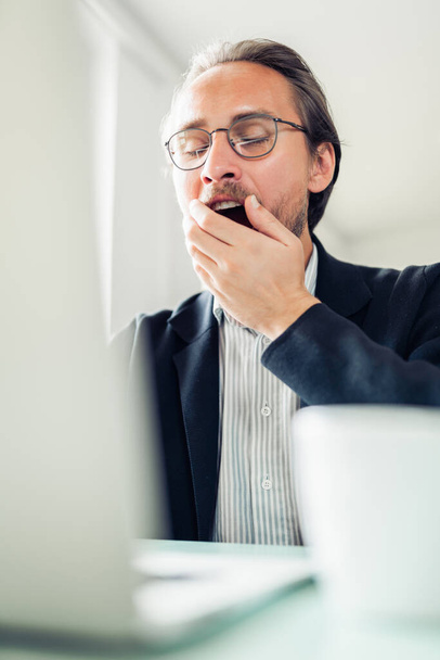 Tired young handsome man is yawning while working at the compute - 写真・画像