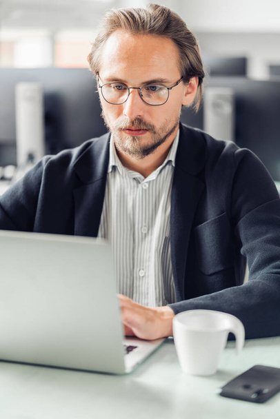 junger Mann sitzt am Schreibtisch und arbeitet an einem Computer. verschwommene Kommunikation - Foto, Bild
