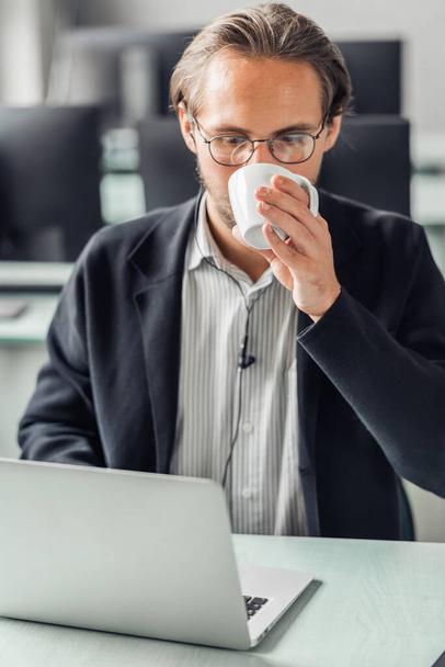 Młody przystojny mężczyzna pijący kawę podczas pracy przy komputerze - Zdjęcie, obraz