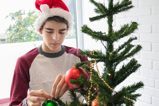Junge mit Weihnachtsmann-Hut schmückt Weihnachtsbaum - Foto, Bild