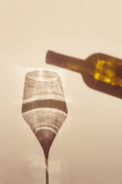 Une longue ombre spectaculaire tombe du verre avec du vin, à côté est l'ombre d'une bouteille de vin. Le concept original de boissons alcoolisées, variétés de vin. Minimalisme, vue de dessus. Espace de copie
 - Photo, image