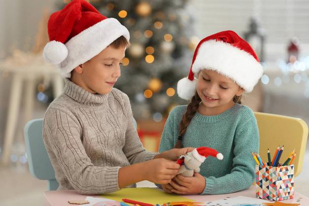 Little children in Santa hats making toy at table indoors. Christmas season - Foto, imagen