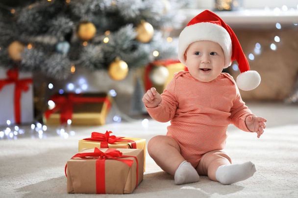 Little baby wearing Santa hat on floor indoors. First Christmas - Fotografie, Obrázek
