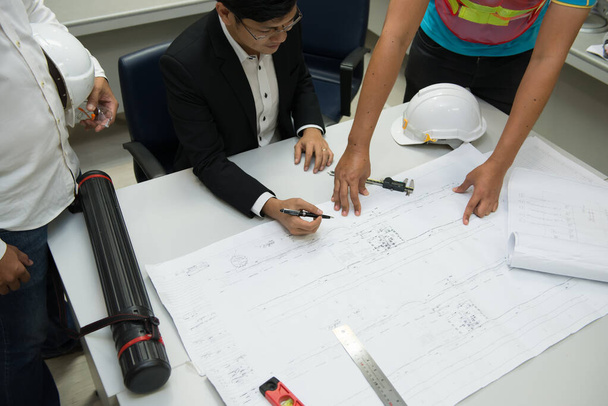 Три азіатських інженери, які шукають паперовий план будівлі, обговорюють проблеми та рішення будівництва в офісі, інженери-замовники скаржаться на зелений будинок не відправляють за графіком
 - Фото, зображення