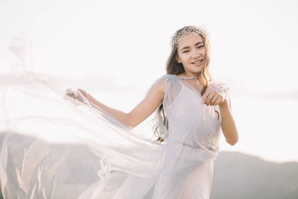 Beautiful girl, happy bride in a white winding in the wind dress watches with a smile - Foto, afbeelding
