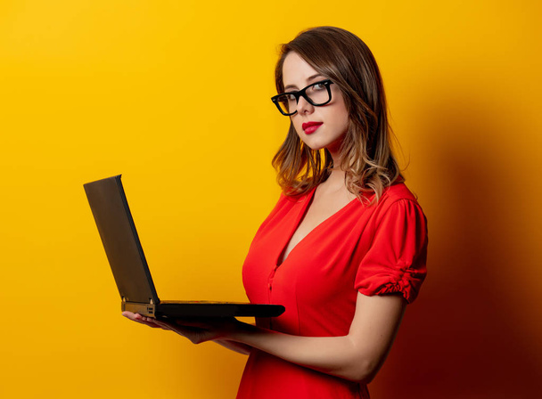Gyönyörű nő piros ruhában laptoppal sárga háton - Fotó, kép