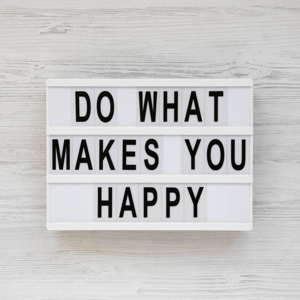 'Do what makes you happy' words on a lightbox on a white wooden  - Foto, Imagen