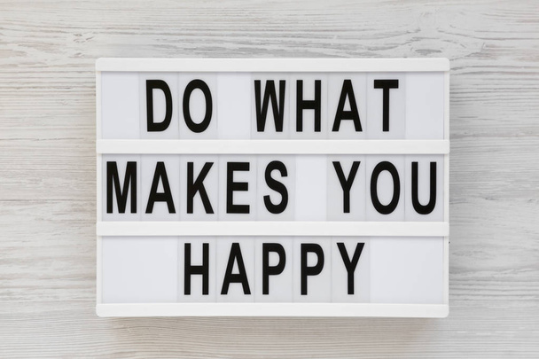 "Tu, was dich glücklich macht" steht auf einem Leuchtkasten auf einem weißen Holzschild  - Foto, Bild