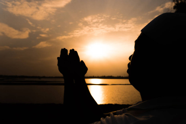 Silhouette junger asiatischer muslimischer Mann, der am Sonnenuntergang betet, Konzept des Ramadan-Festivals - Foto, Bild