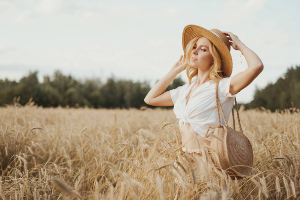 Joven mujer feliz en el campo de trigo. Retrato de una hermosa chica rubia en un campo en blusa blanca y sombrero de paja. concepto belleza y salud. naturaleza de verano
 - Foto, imagen