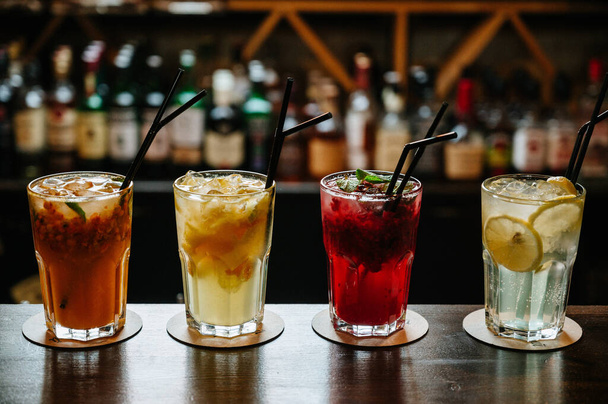 Diversi tipi di bevande estive in bicchieri, cubetti di ghiaccio e fetta di frutta sul tavolo scuro allargato
. - Foto, immagini