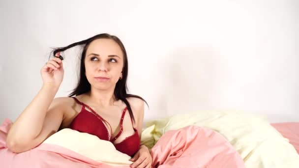A young attractive woman in a lingerie twirls her hair thoughtfully and decides to entertain herself with a big dildo in a bed. - Imágenes, Vídeo