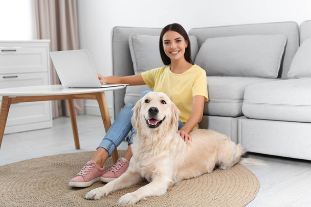 Young woman and her Golden Retriever dog in living room - Фото, изображение