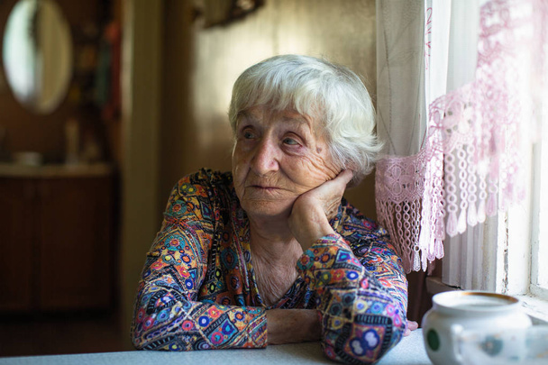 Elderly woman sitting at a table in the house. - Photo, Image