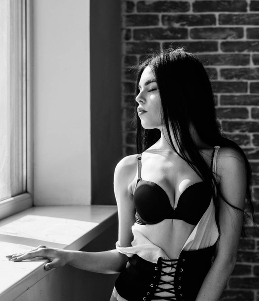 Passionate mysterious lover. Enjoying morning sunlight. Sensual girl sexy breasts relaxing near windowsill. Attractive female lingerie just relaxing at home. Could not be better. Enjoying her beauty - Zdjęcie, obraz