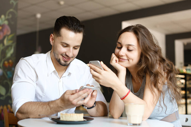 Молода жінка сидить з чоловіком і використовує смартфон у кафе
. - Фото, зображення