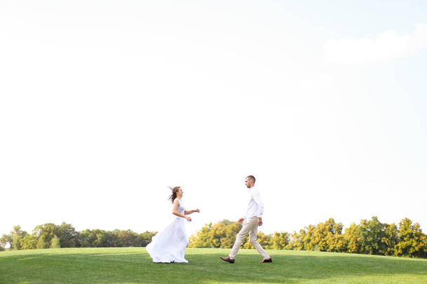 Happy bride and groom running to each other on grass in white sky background. - Fotografie, Obrázek