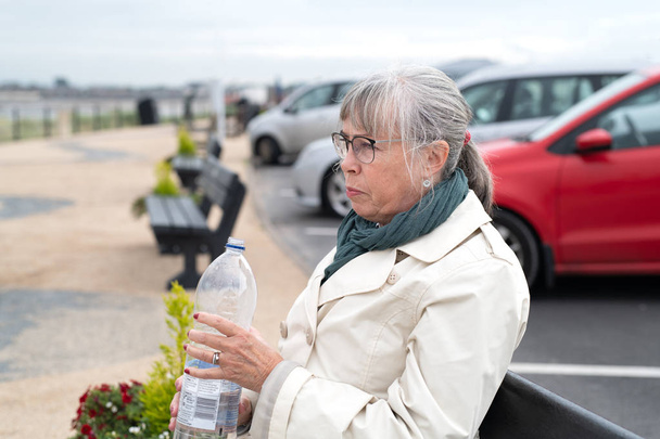 Yaşlı kadın kasabada su içiyor. - Fotoğraf, Görsel
