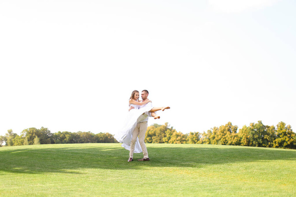 Caucasian groom holding bride on grass in white sky background. - Fotografie, Obrázek