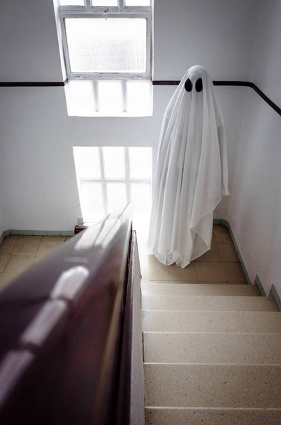 Duch zakrytý bílým přízračným prostěradlem na schodech opuštěné psychiatrické léčebny. Halloween Concept - Fotografie, Obrázek