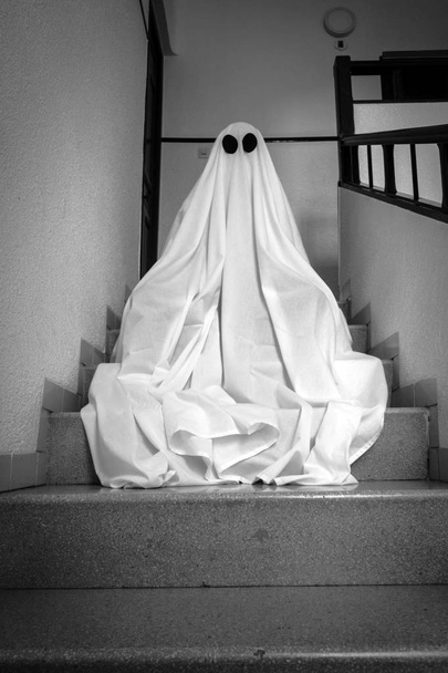 Duch zakrytý bílým přízračným prostěradlem na schodech opuštěné psychiatrické léčebny. Halloween Concept - Fotografie, Obrázek