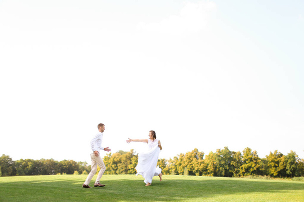 Groom and happy bride running and playing on grass. - Zdjęcie, obraz