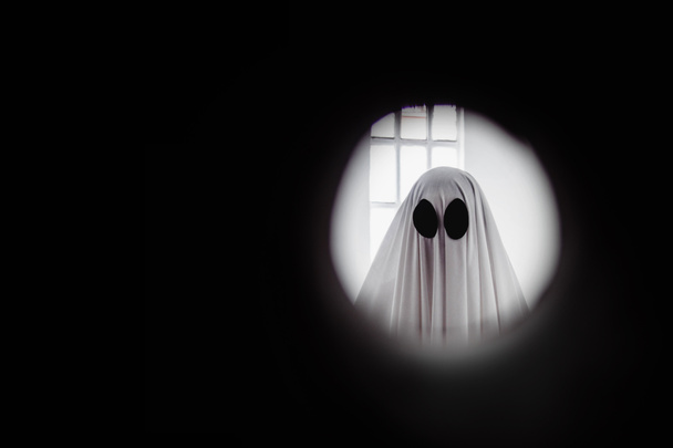 Ghost covered with a white ghost sheet behind the door through the peephole. Halloween Concept - Foto, immagini