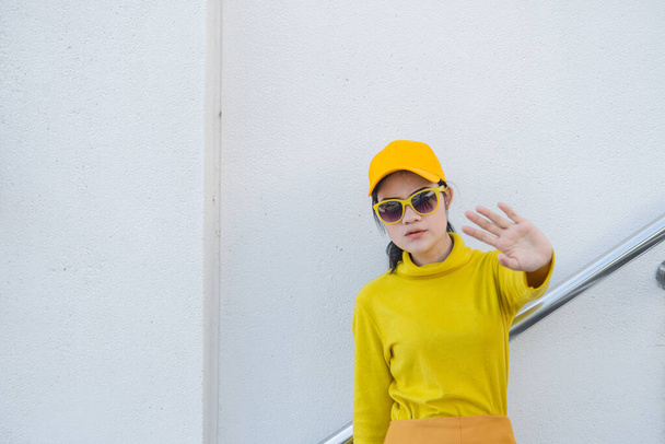 Portrait of beautiful asian woman in yellow cloths make hand stop,Hipsters girl wear yellow hat on stair for take a picture,Thailand people in yellow tone style - Foto, imagen