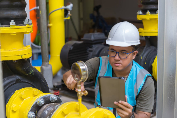 Asian engineer wearing glasses working in the boiler room,maintenance checking technical data of heating system equipment,Thailand people - Foto, Imagem