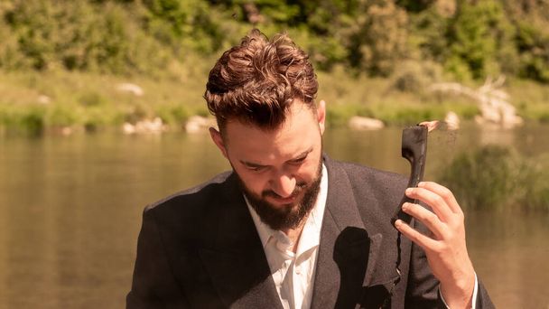 A businessman in a suit during vacation holds in his hand a phone that is on fire. Toning. The concept of hated work, humor about the technical support hotline or non-observance of safety measures - Foto, afbeelding