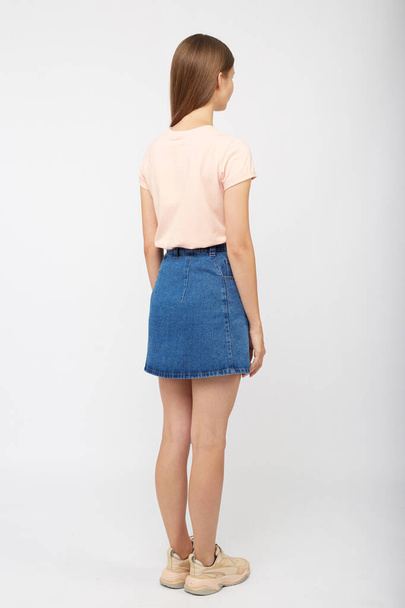 Teenager girl in a denim blue skirt on a white background. - Fotó, kép