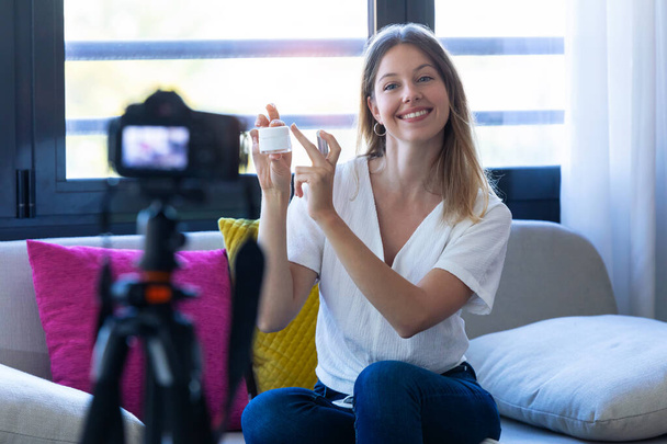 Pretty young woman blogger holding beauty products and smiling while making social media video - Foto, afbeelding
