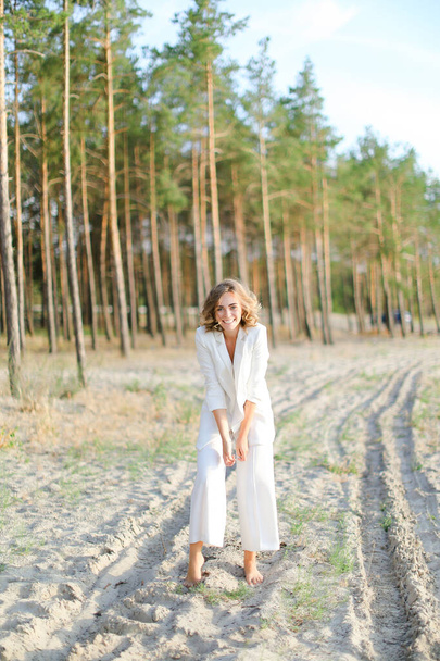 Ξανθιά καυκάσια γυναίκα που περπατάει στην παραλία και φοράει λευκά ρούχα. - Φωτογραφία, εικόνα