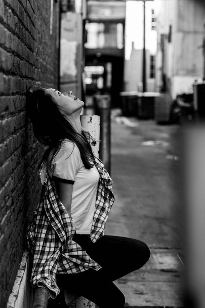 Woman with long hair on the street. Black and white portrait. Brick wall behind model. Street style fashion outfit. Urban lifestyle outfit. Plaid shirt, white t-shirt. Rebel girl. Different emotions. - Фото, изображение