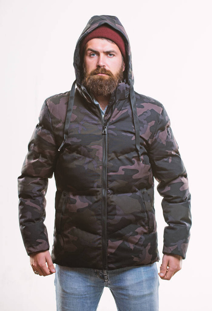 Comfortable winter outfit. Winter stylish menswear. Man bearded stand warm camouflage pattern jacket parka isolated on white background. Hipster winter fashion. Guy wear hat and black winter jacket - Fotó, kép