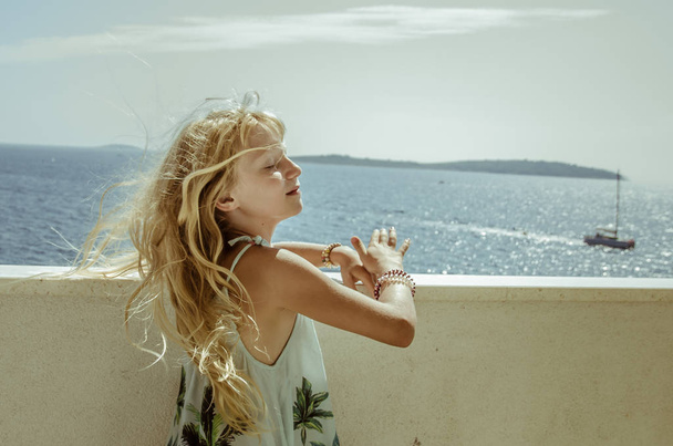 schattig meisje in winderig weer met golvend lang blond haar van waait wind met in de zomer vakantie sfeer - Foto, afbeelding