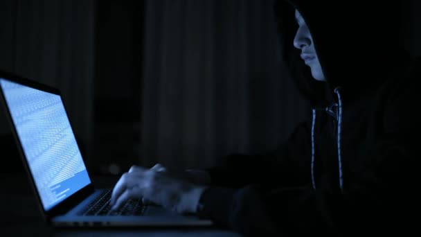 Hacker's hacking into the computer network. A young guy in a dark room typing on a laptop.  Hacker with a laptop. E-the robber. Lonely teen chatting online. Computer criminal. 4K footage. - Filmmaterial, Video
