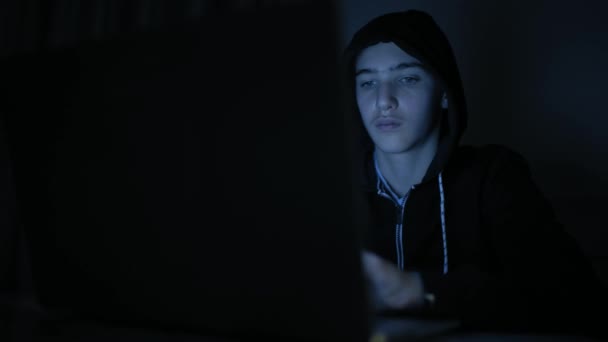 Hacker's hacking into the computer network. A young guy in a dark room typing on a laptop.  Hacker with a laptop. E-the robber. Lonely teen chatting online. Computer criminal. 4K footage - Filmmaterial, Video