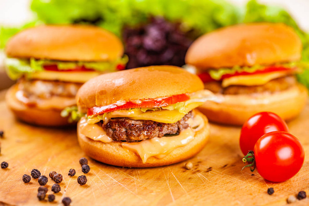 Três mini hambúrgueres com costeletas de carne, tomates e queijo em tábua de madeira
 - Foto, Imagem