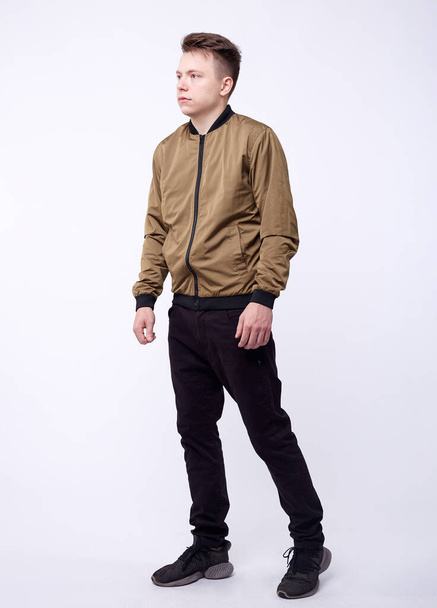 Young man in jeans, shiny nylon gold bomber jacket on white background. - Foto, immagini
