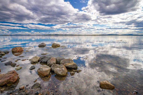 Kameny na břehu zátoky Kandalaksha v Bílém moři. Mraky a obloha se odrážejí ve vodě - Fotografie, Obrázek