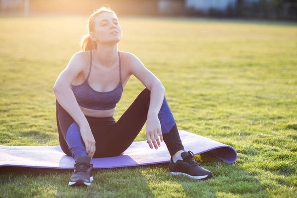 Jovem mulher esportiva em roupas esportivas sentado no tapete de treinamento b
 - Foto, Imagem