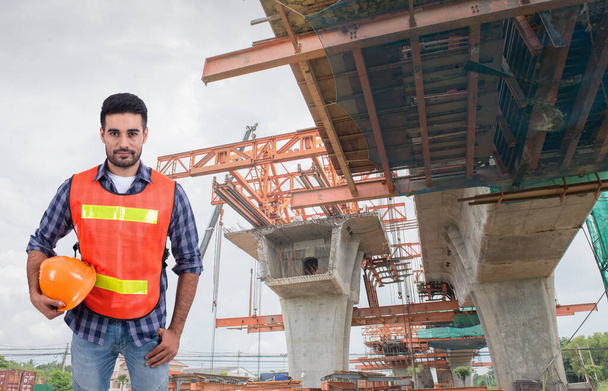 Civil engineer holding a helmet on a large bridge under construction background - Fotó, kép