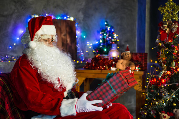 Santa claus holding gift box at home,Sit on chair think about plan for sent gift box for give children - Foto, afbeelding